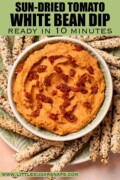 Labelled white bean dip with sun-dried tomato served with seeded breadsticks.