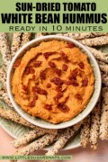 Labelled white bean hummus with sun-dried tomato served with seeded breadsticks.