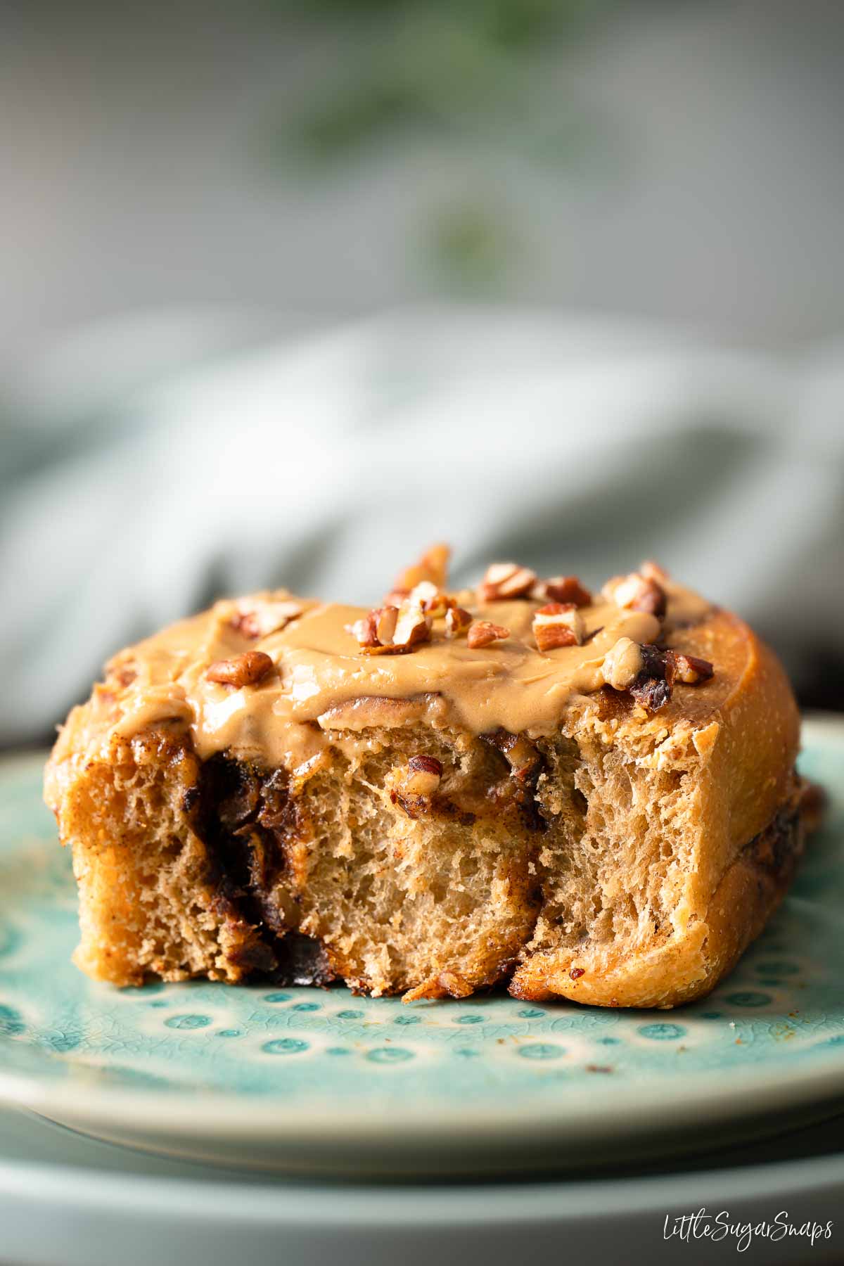 A part eaten date and coffee cinnamon roll with coffee flavoured glaze and chopped pecan nuts.