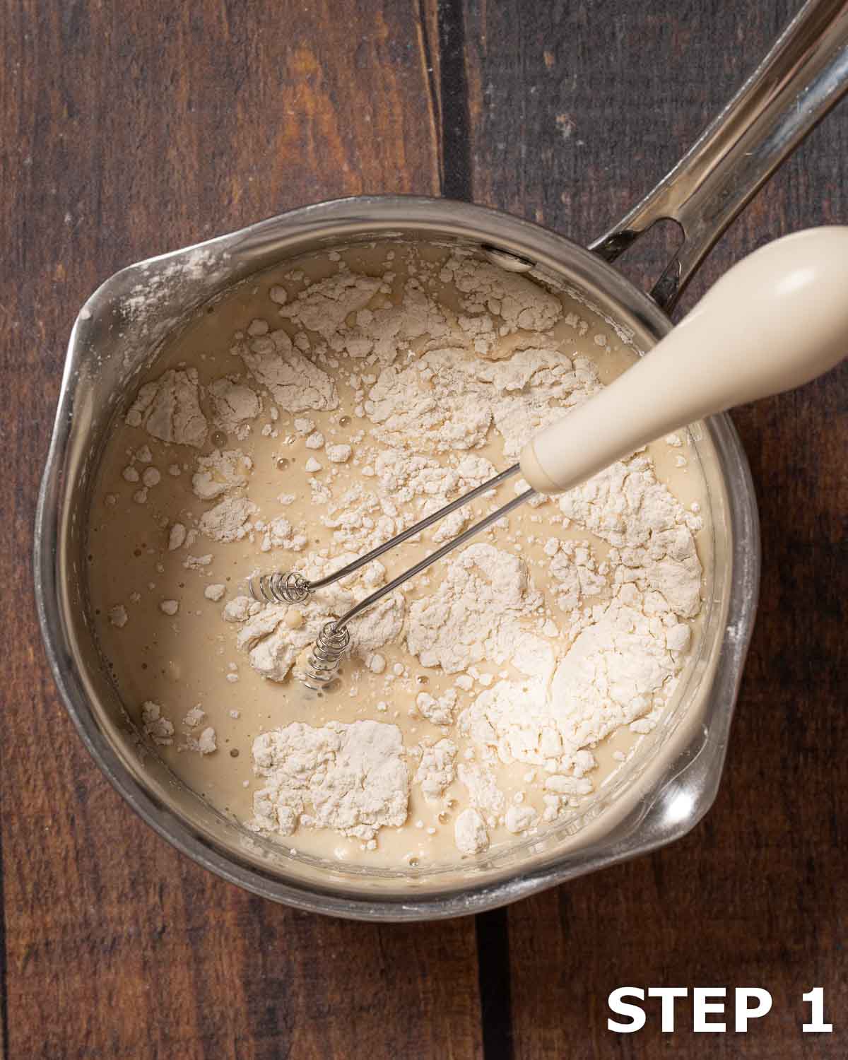 Flour and milk in a small saucepan with a small handheld whisk.