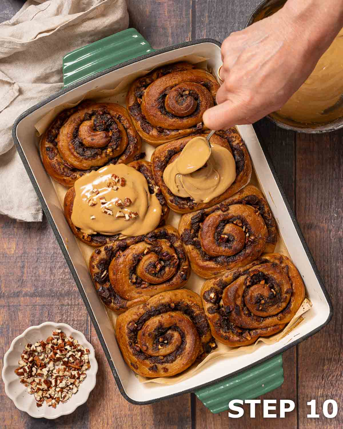 A person spreading coffee glaze over cinnamon coffee rolls in a baking dish.