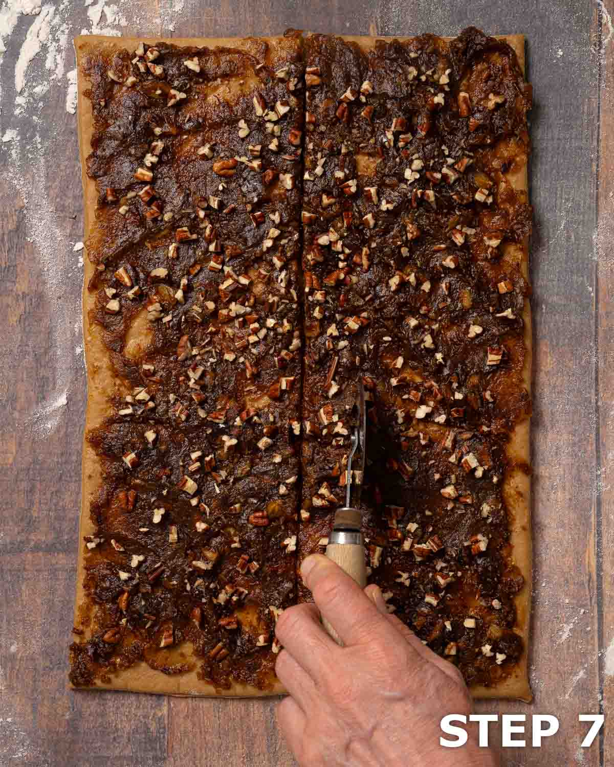 Dough rolled out and topped with dates and pecan nuts being cut into strips using a pizza wheel.