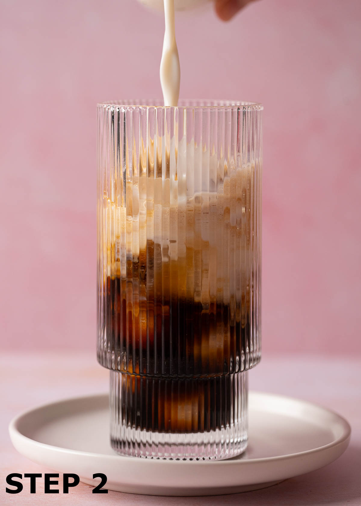 Milk being poured into a glass containing ice and espresso coffee.