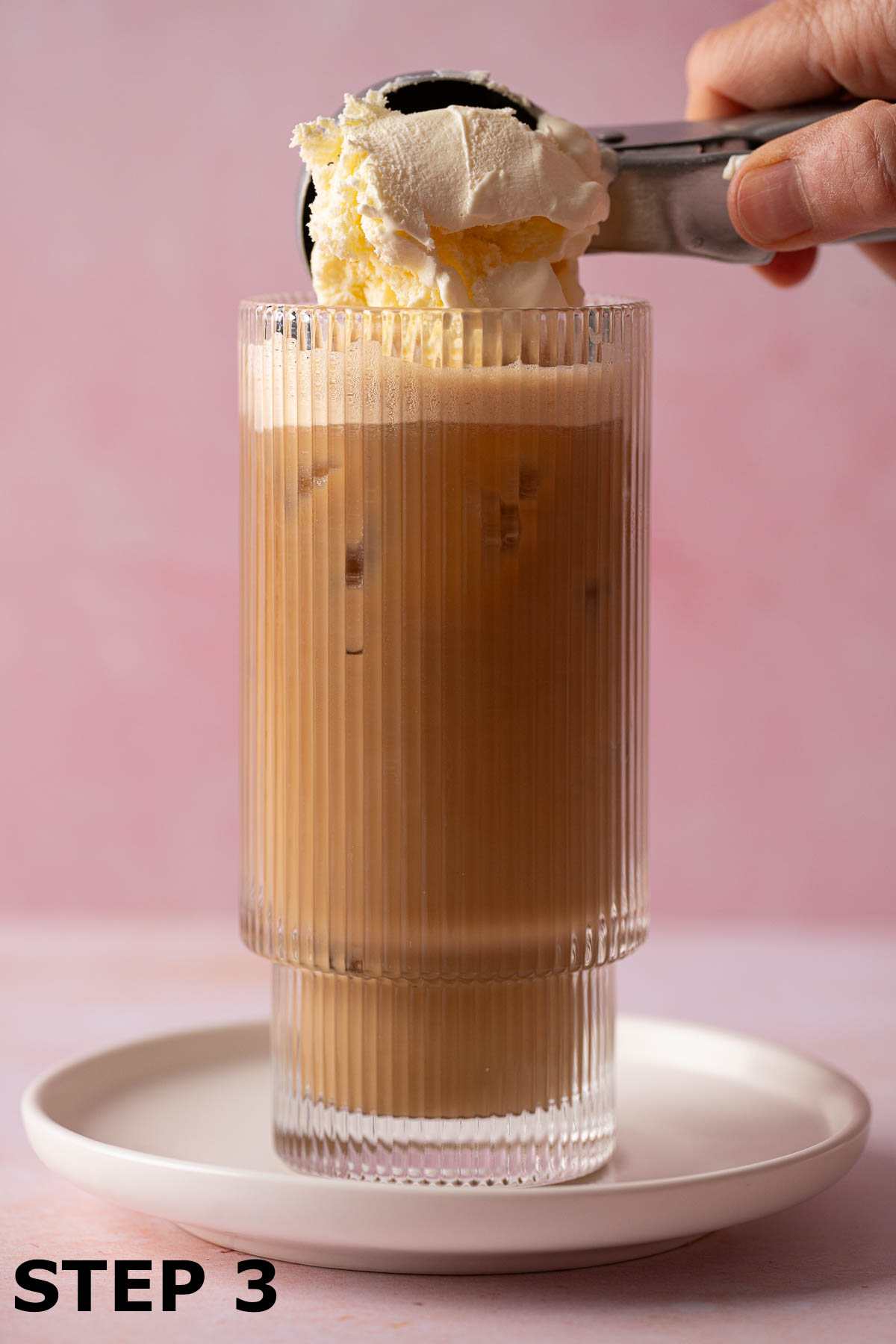 A scoop of ice cream being added onto the top of an iced latte.