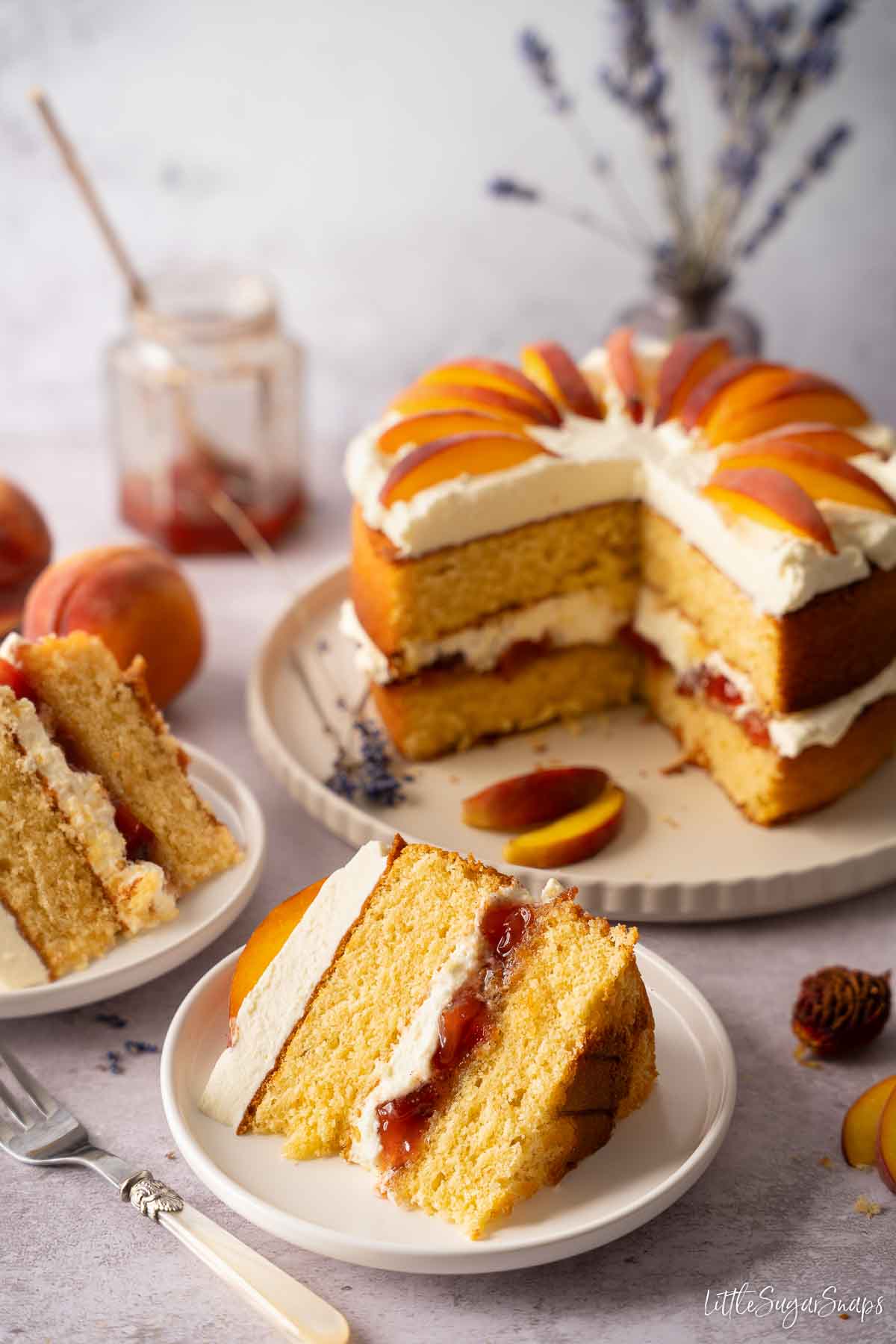 A plated slice of peach cream cake with the rest of the cake in the background.