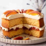 A cut into peaches and cream cake with peach jam and fresh peach slices.