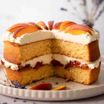 A cut into peaches and cream cake with peach jam and fresh peach slices.