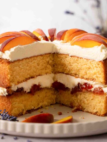 A cut into peaches and cream cake with peach jam and fresh peach slices.
