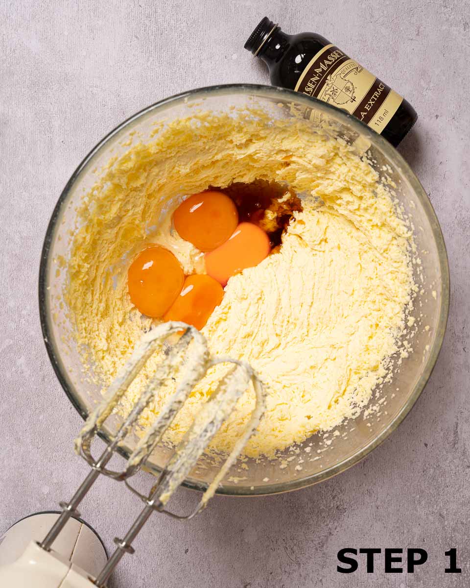 Egg yolks and vanilla extract in a mixing bowl with creamed butter and sugar.