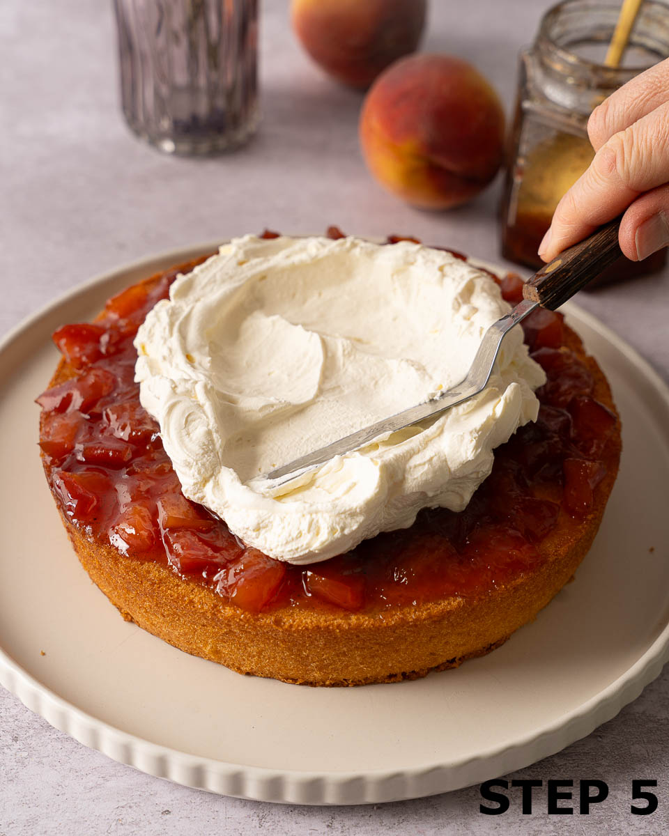 A person spreading fresh cream over jam on the base of a sponge cake.