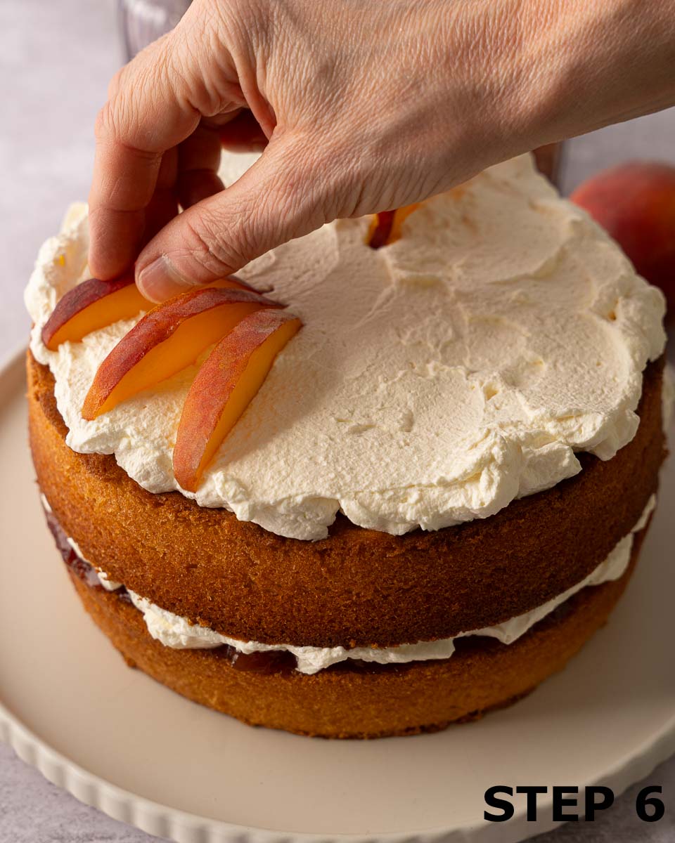 A person decorating the top of a cream cake with wedges of peach.
