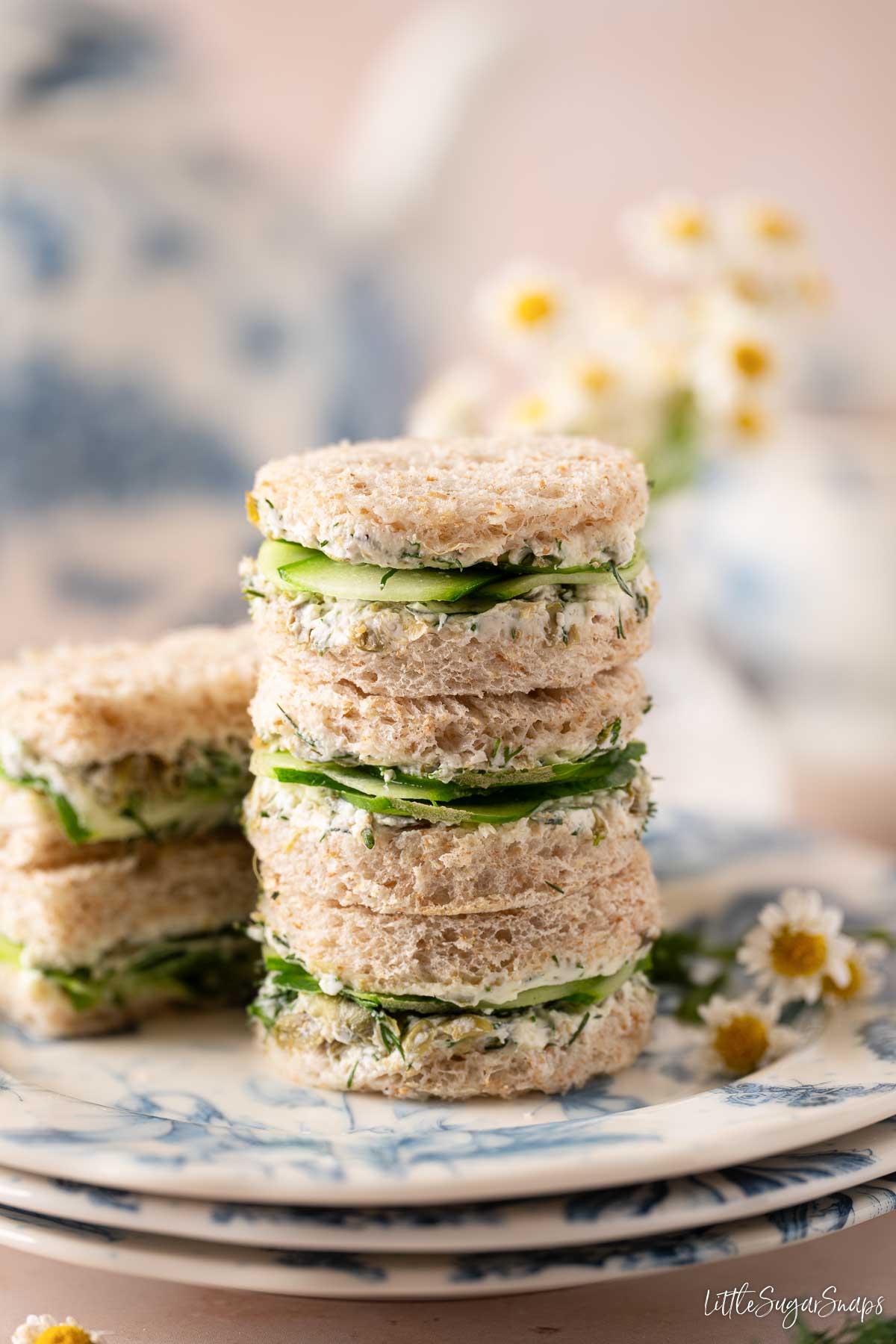 Three circular cucumber dill sandwiches on a plate with finger sandwiches behind them.