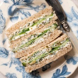 Three cucumber finger sandwiches on a plate with a knife beside them.