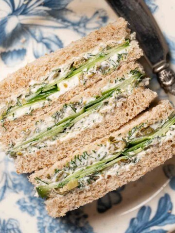 Three cucumber finger sandwiches on a plate with a knife beside them.