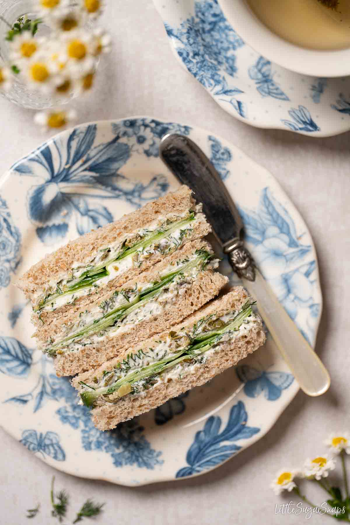 Three cucumber finger sandwiches on a plate with a knife beside them.