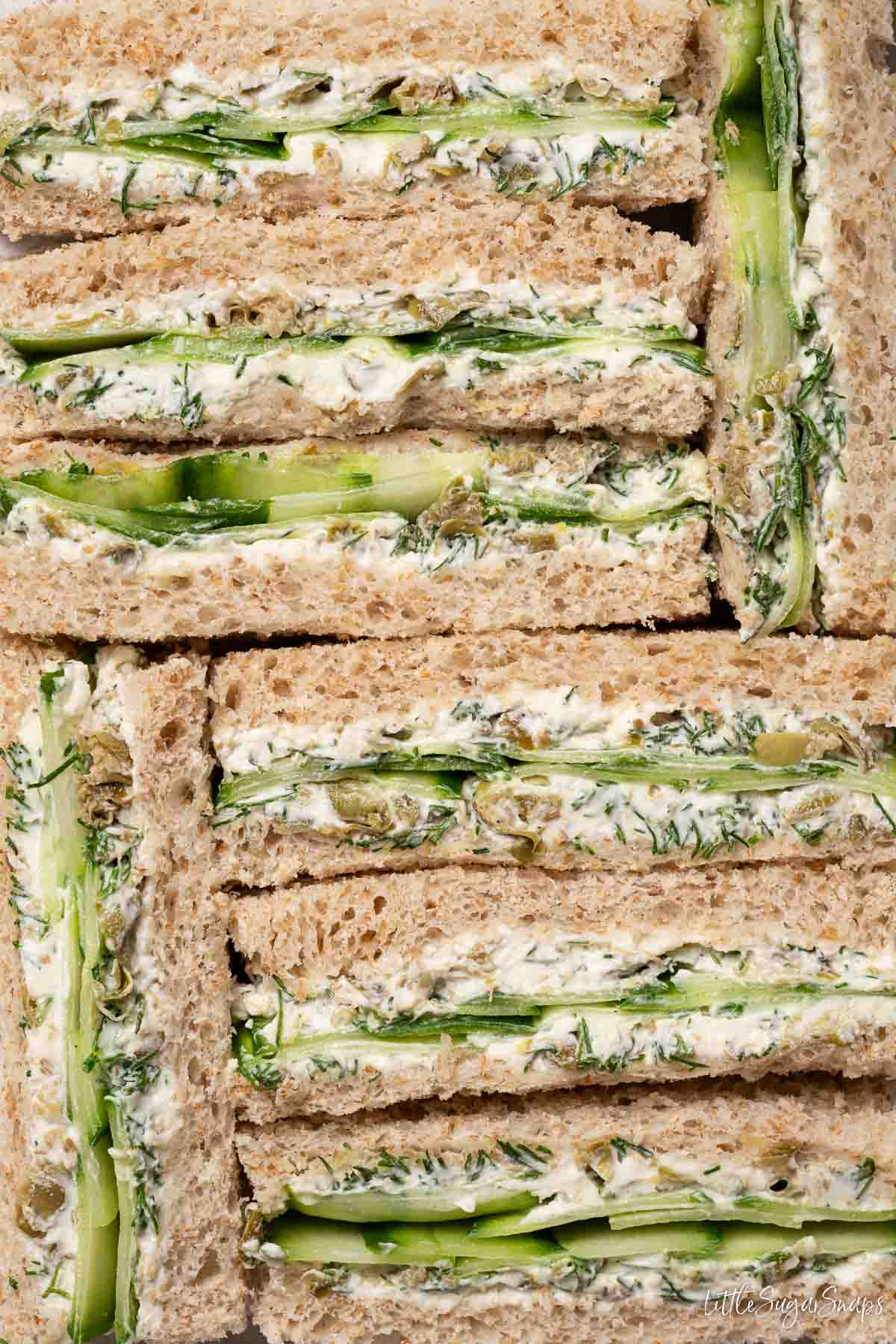 Cucumber cream cheese finger sandwiches stacked closely together.