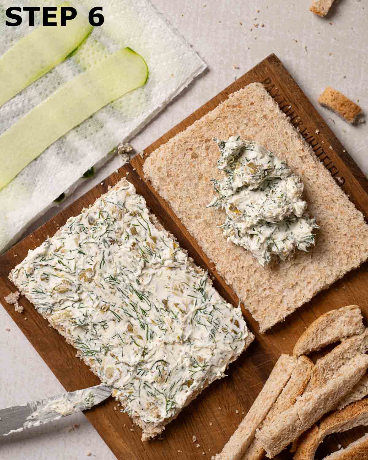 Cream cheese sandwich filling being spread over brown bread.