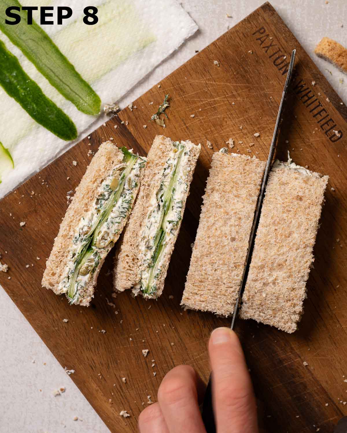 A person cutting afternoon tea cucumber sandwiches into fingers.