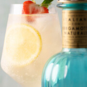 An Italicus spritz cocktail with lemon and strawberry garnish behind a bottle of Italicus liqueur.