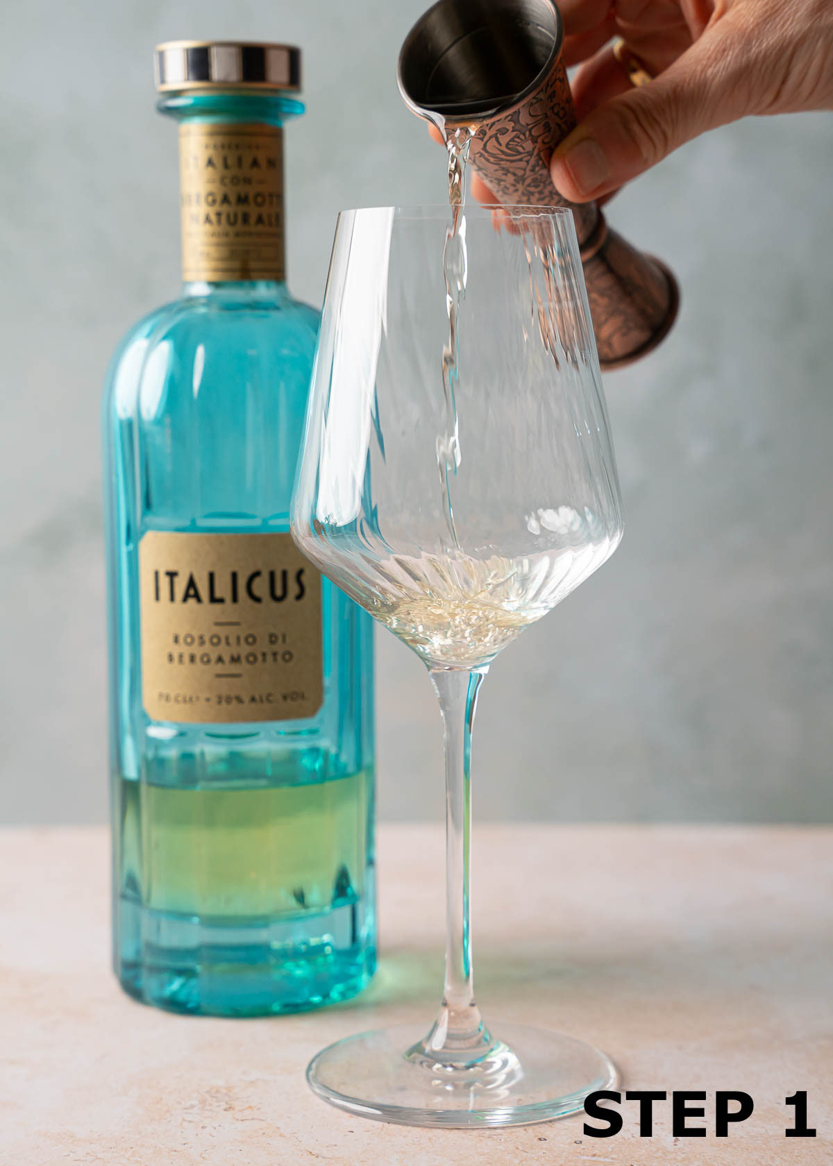 A person pouring Italicus liqueur into a ribbed wine glass from a cocktail jigger.