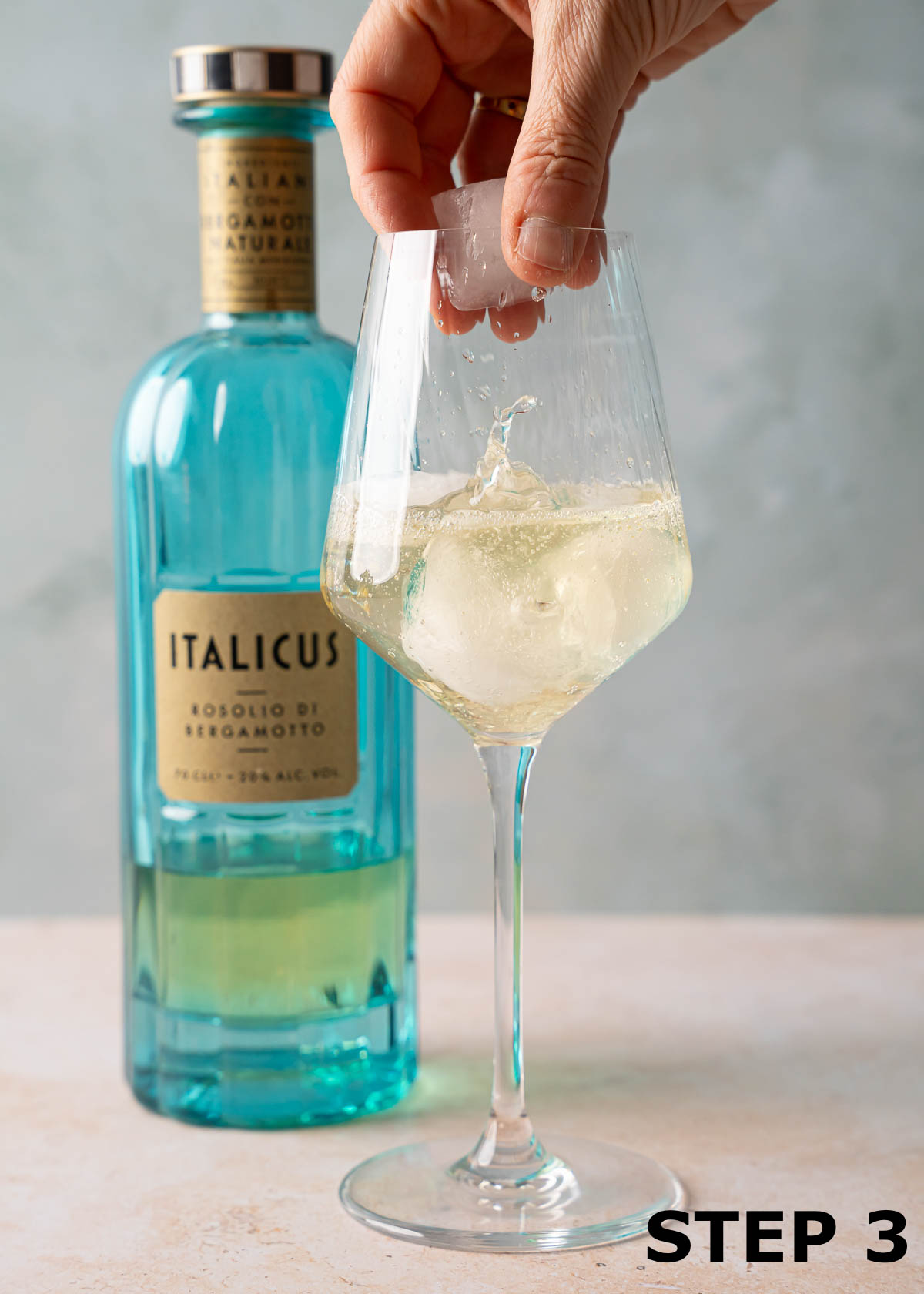 Ice being add to a sparkling Italicus drink in a wine glass.