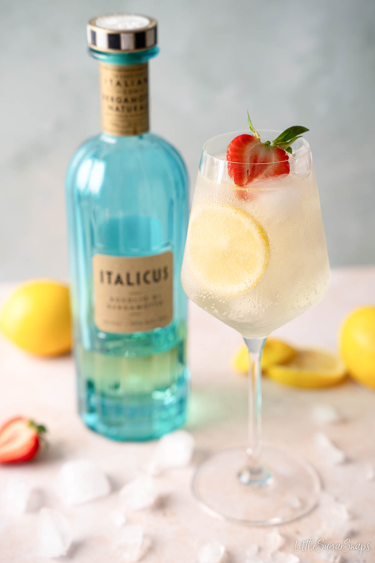 Italicus spritz with lemon and strawberry garnish with a bottle of Italicus liqueur.
