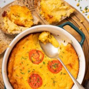 Part-served baked cheese pudding topped with sliced tomato and chives with toast on the side.