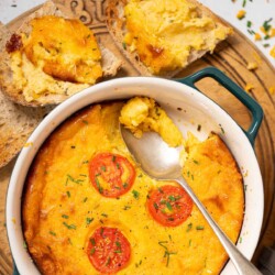 Part-served baked cheese pudding topped with sliced tomato and chives with toast on the side.