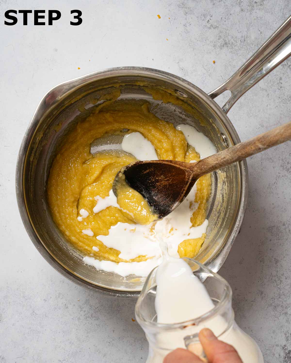 Milk being poured into a butter and flour roux.