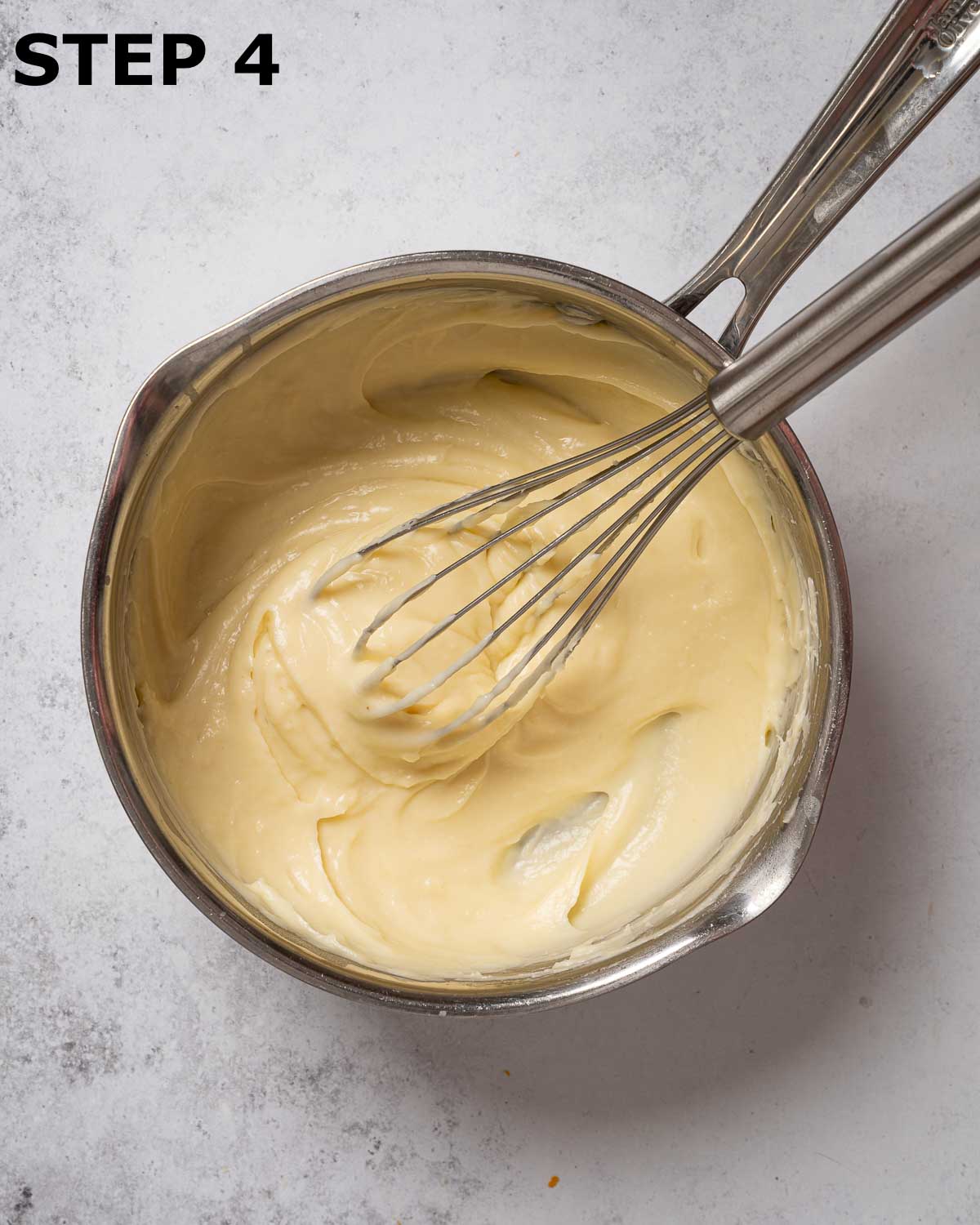 White sauce in a pan with a balloon whisk resting in it.