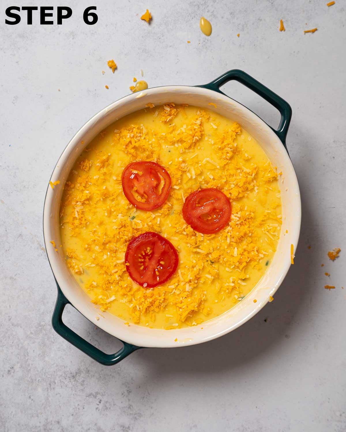 The batter for Rutland cheese savoury in a round dish topped with grated cheese and tomato before being baked.