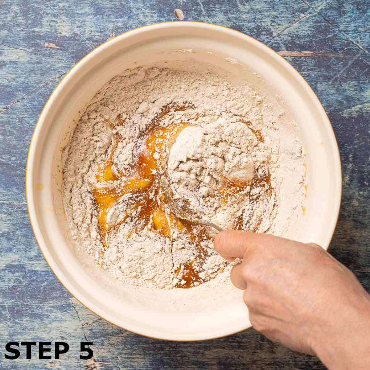 A person mixing flour and spices into dough for chewy pumpkin cookies.