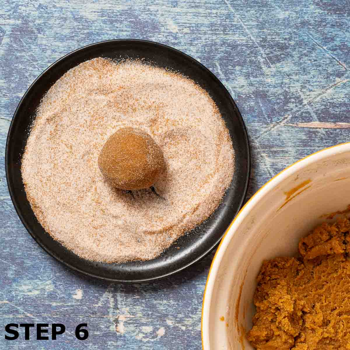 A ball of pumpkin pie spice cookie dough being rolled in spiced sugar.